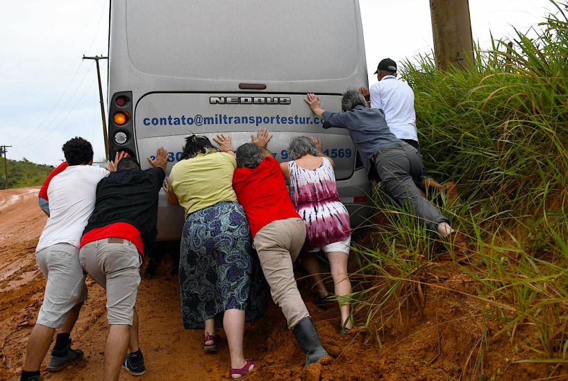 A group of people pushing the back of a bus that is stuck in the mud.